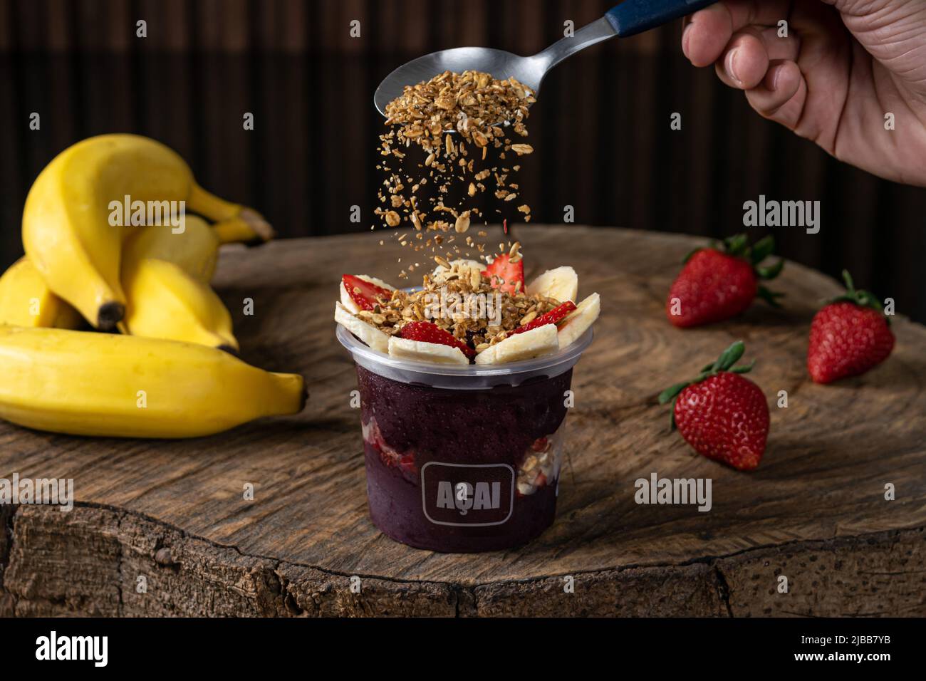 Délicieuse crème brésilienne açaí, dans une tasse en plastique avec garniture fraise, banane et granola, dans un fond rustique en bois. Smoothie d'açai d'été Banque D'Images