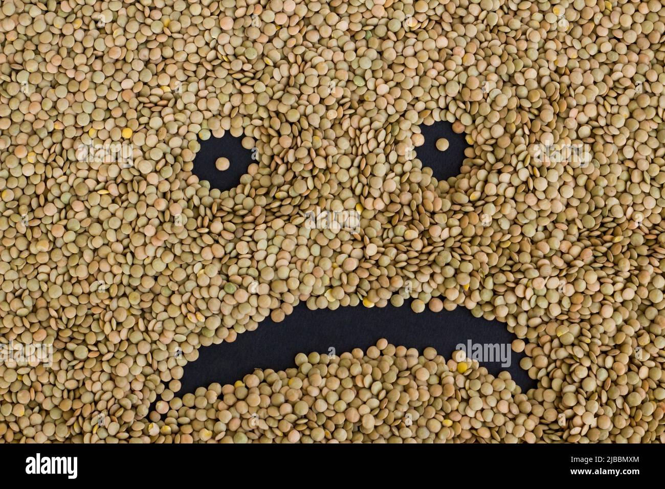 Triste visage emoji avec des lentilles vertes sèches sur la surface noire, concept de récolte Banque D'Images