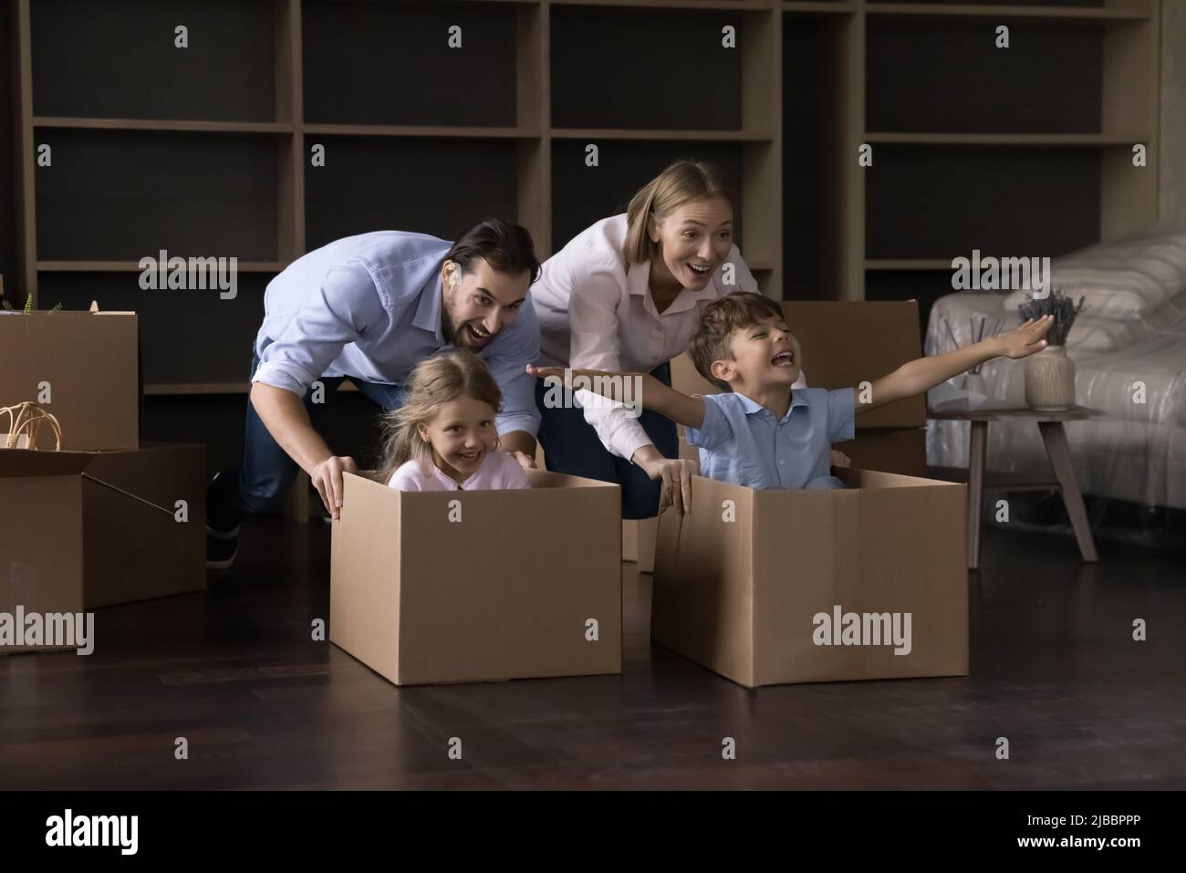 Les parents jouent la course poussent leurs frères et sœurs assis dans des boîtes en carton Banque D'Images