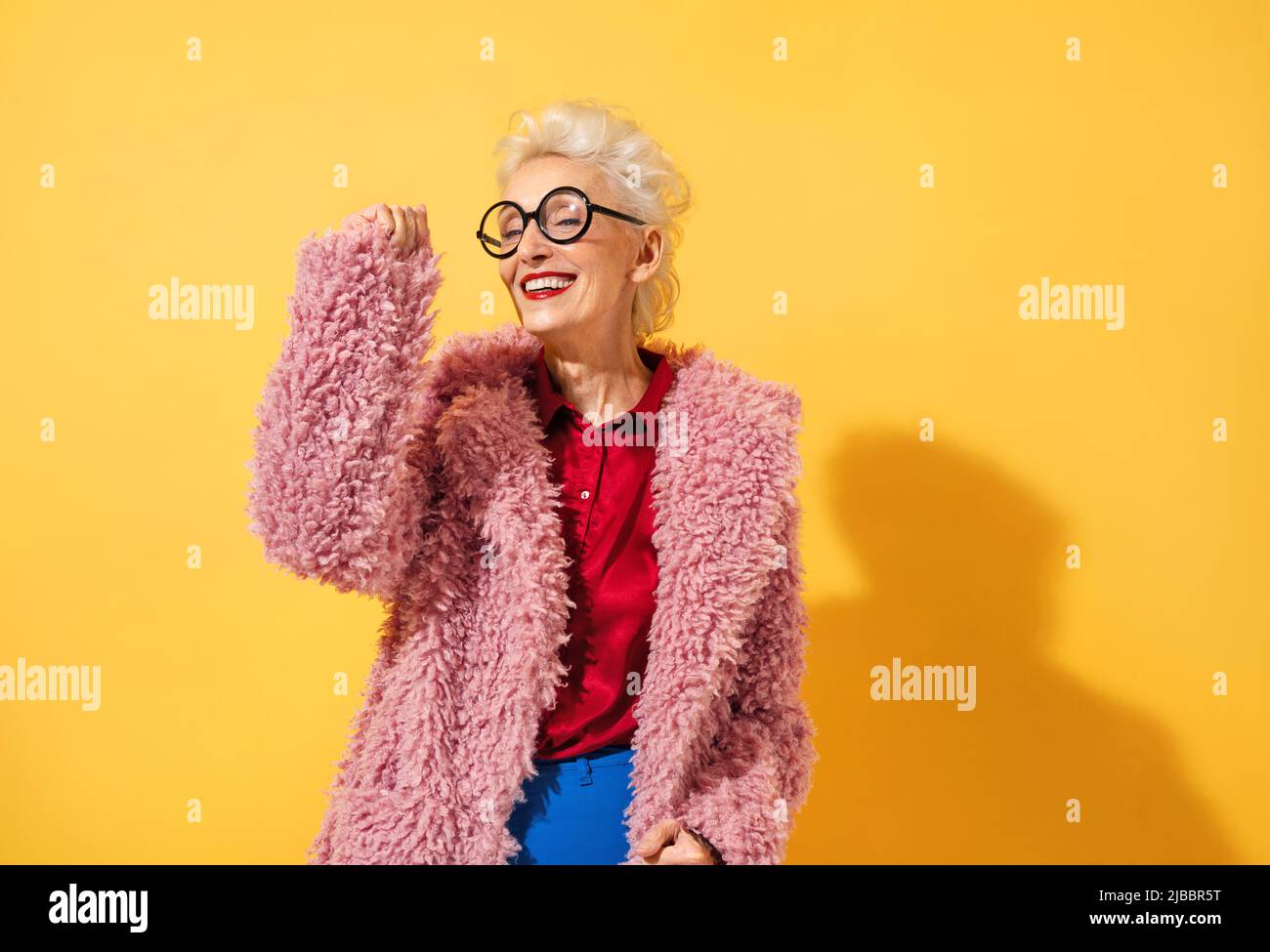 Bonne et ludique femme mûre dansant, souriant et s'amusant. Photo d'une femme âgée de plus de 70 ans avec une tenue élégante sur fond jaune Banque D'Images
