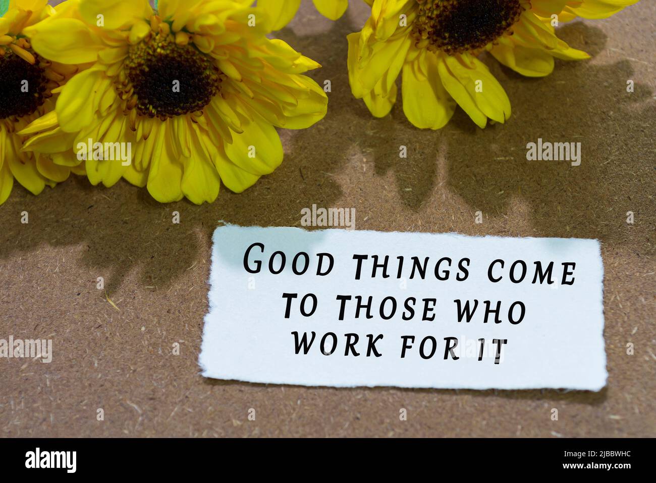 Citation motivationnelle sur papier blanc déchiré avec tournesol sur fond de table en bois - de bonnes choses viennent à ceux qui travaillent pour elle. Banque D'Images