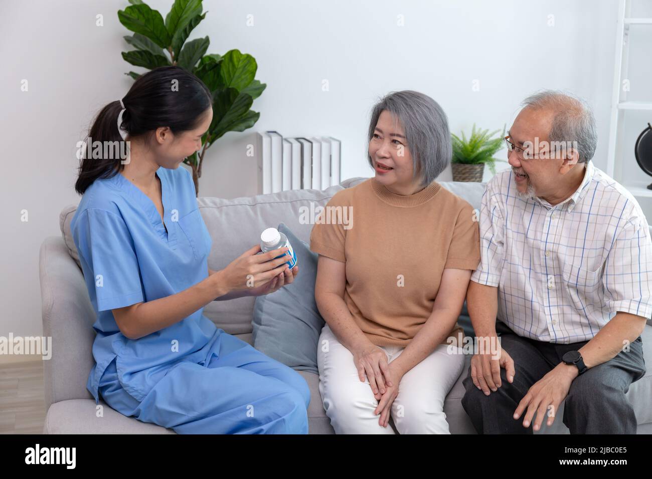 Jeune infirmière prenant soin des personnes âgées assises sur un canapé. Une femme qui aide les patients âgés tout en souriant. Banque D'Images