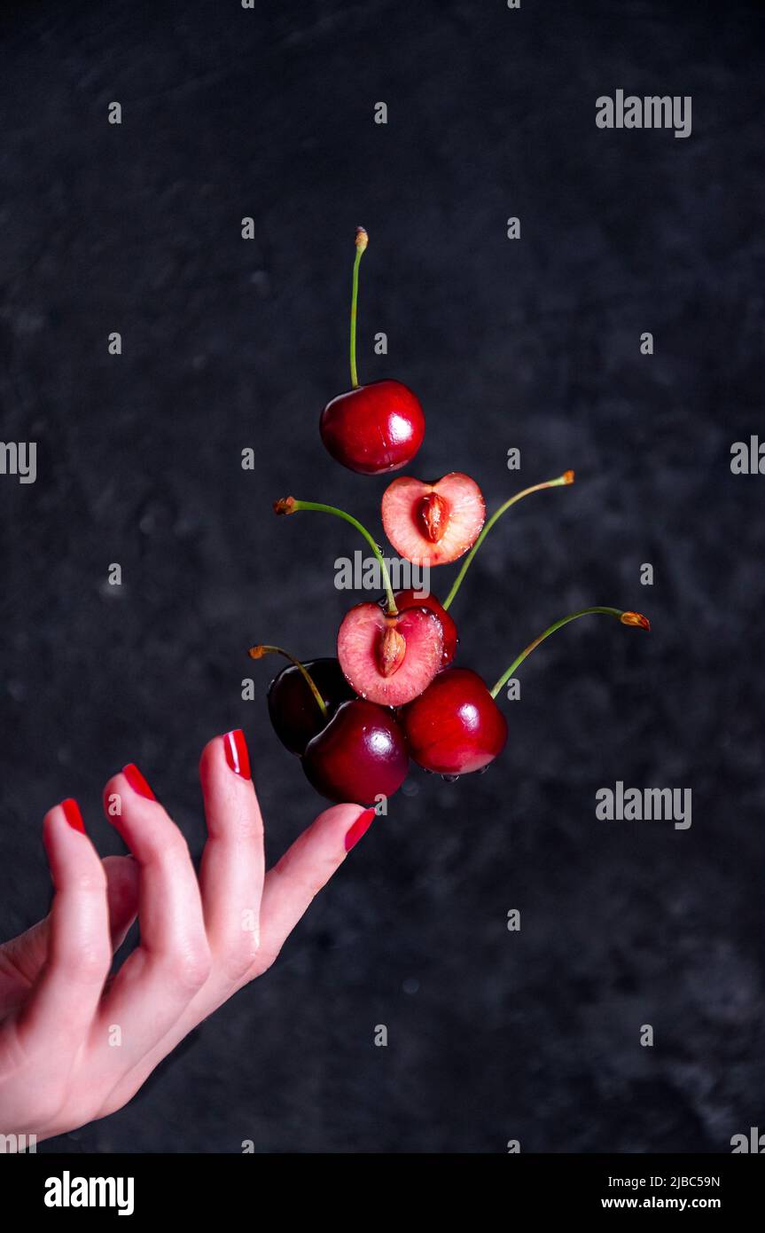 Gros plan composition de la lévitation Cherries sur le doigt de la femme sur le fond sombre Banque D'Images