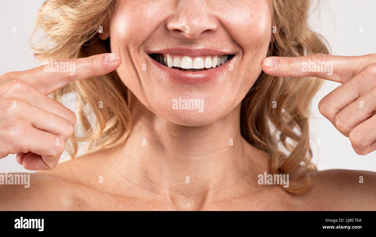 Soins buccaux. Belle femme d'âge moyen pointant vers son sourire avec les doigts Banque D'Images
