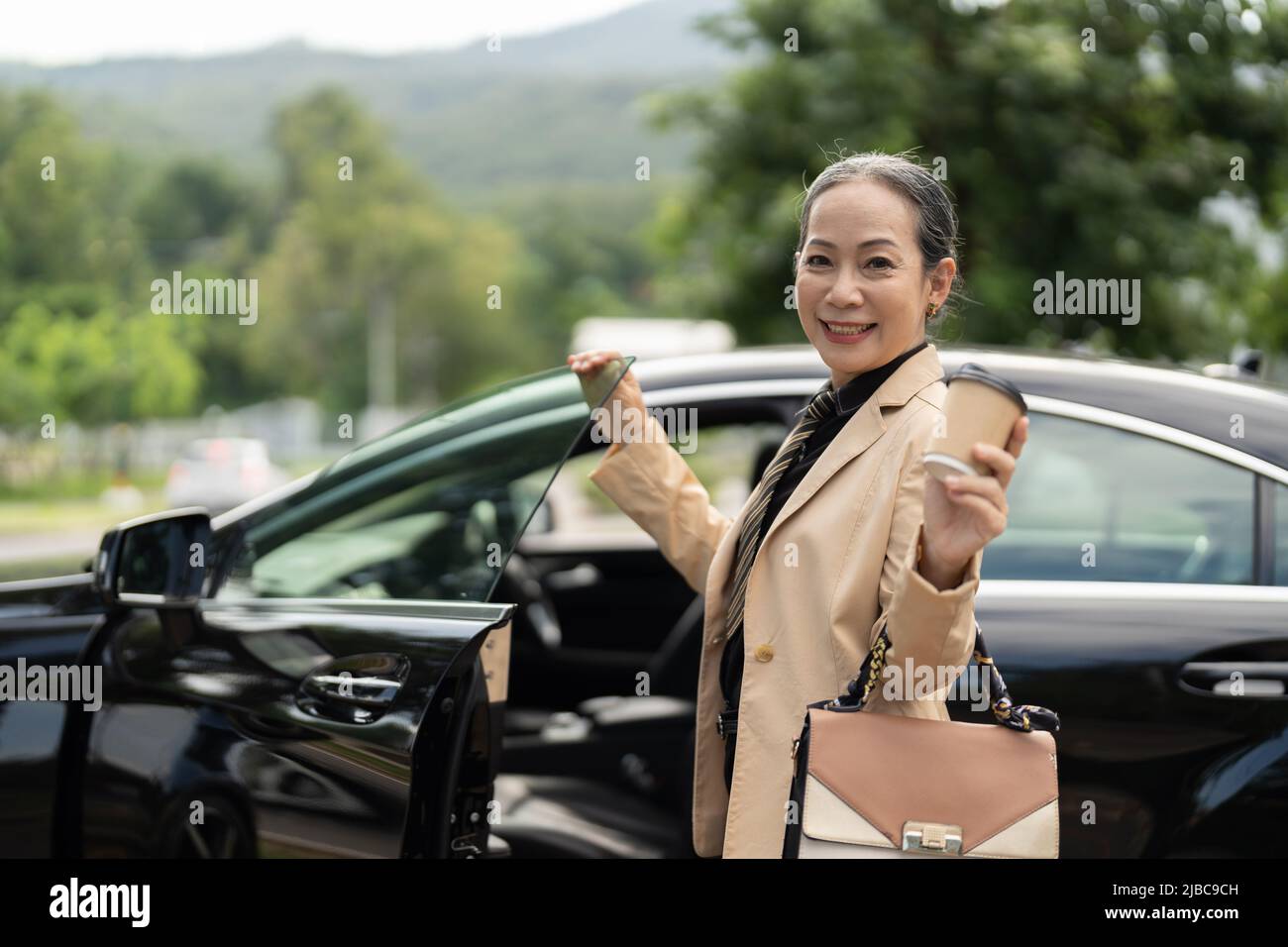 Une femme d'affaires confiante débarque dans une voiture de luxe avec un regard souriant sur l'appareil photo Banque D'Images