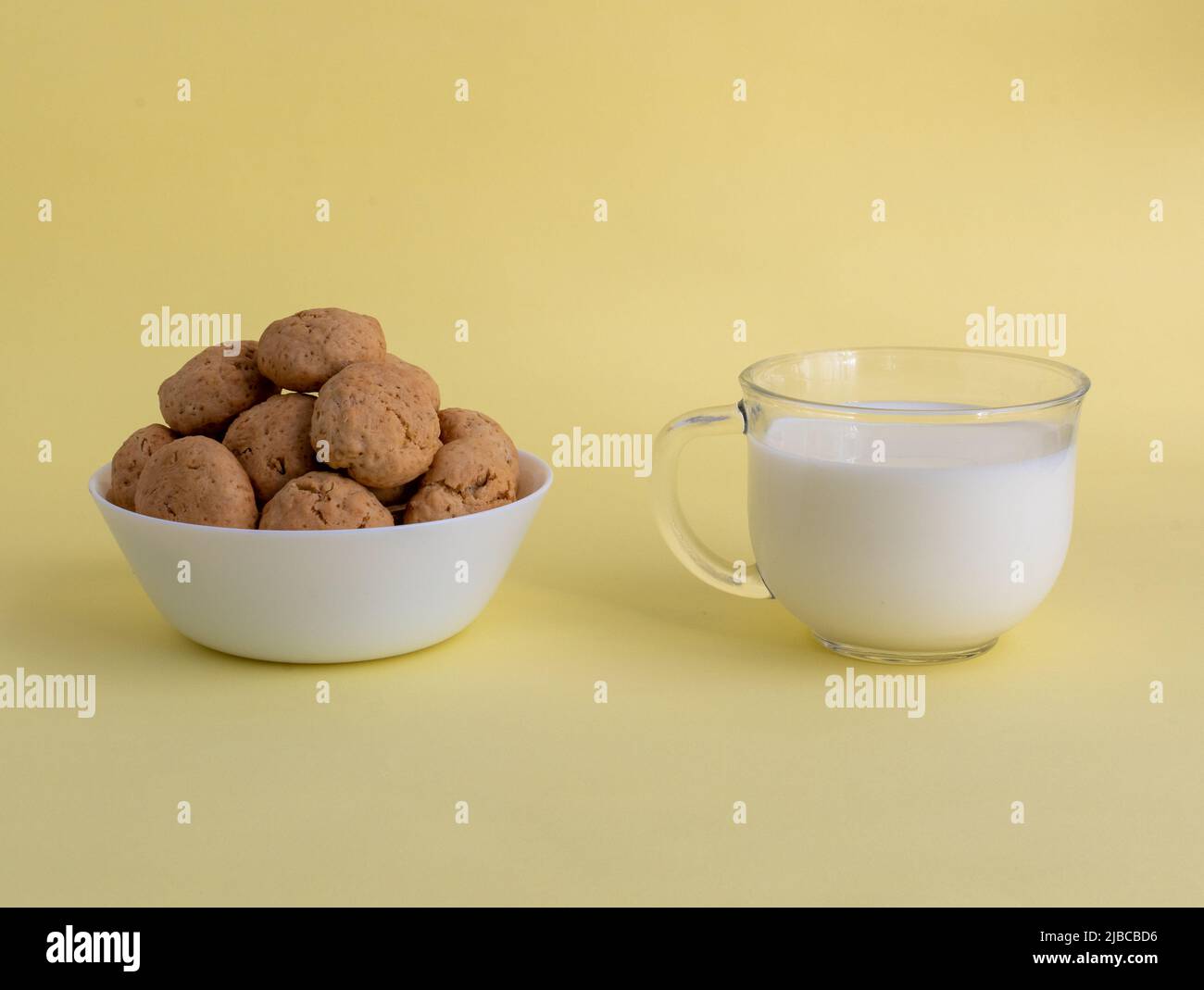 Biscuits aux flocons d'avoine sur une assiette blanche, lait blanc dans un verre transparent vue latérale sur un fond jaune. Photo de haute qualité Banque D'Images