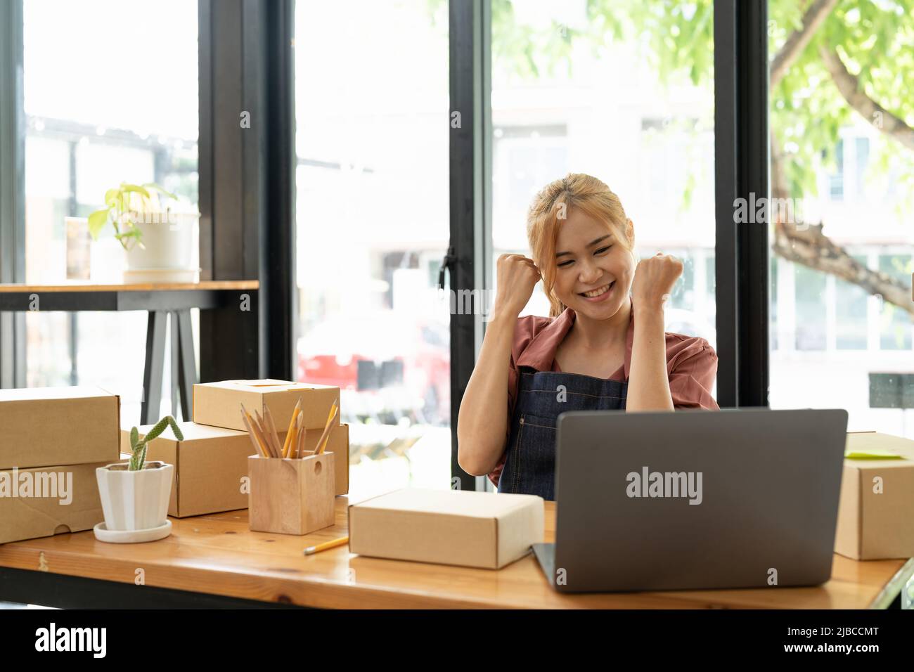 Happy Young Asian femme entrepreneur, Smile pour le succès de vente après avoir vérifié la commande de magasin en ligne dans un smartphone à la maison de bureau, concept Banque D'Images