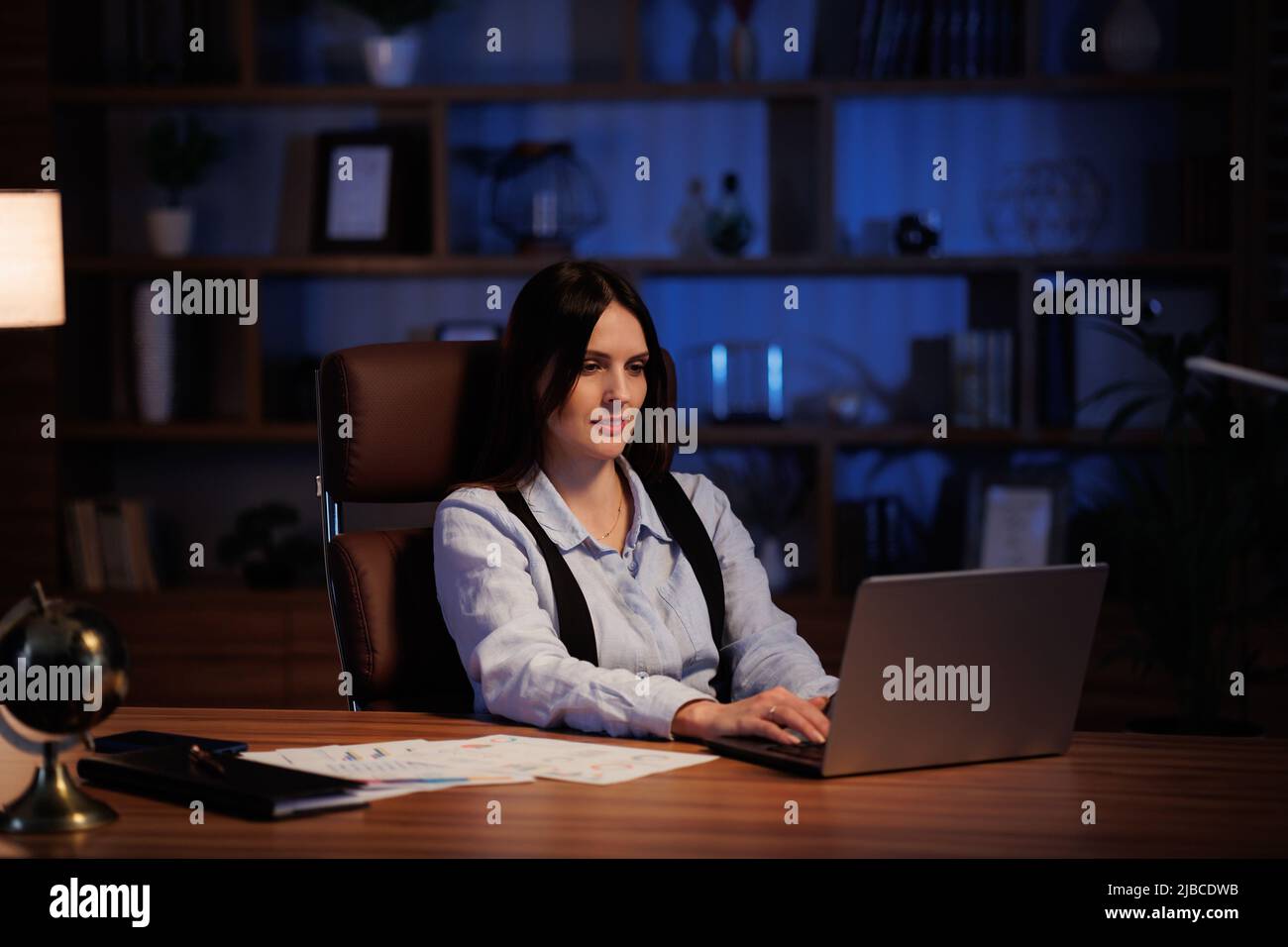 Jeune femme travaillant avec un ordinateur portable au bureau. Un employé de bureau analyse des graphiques et des graphiques, travaille de manière excessive pendant qu'il est assis au bureau jusque tard dans la nuit. Vidéo cinématographique Banque D'Images