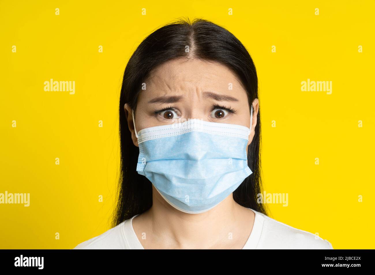 Peur de la pandémie adulte femme asiatique portant un masque médical coronavirus ou prévention de la monkeypox. Charmante femme d'âge moyen en t-shirt blanc et masque médical sur fond jaune. Banque D'Images