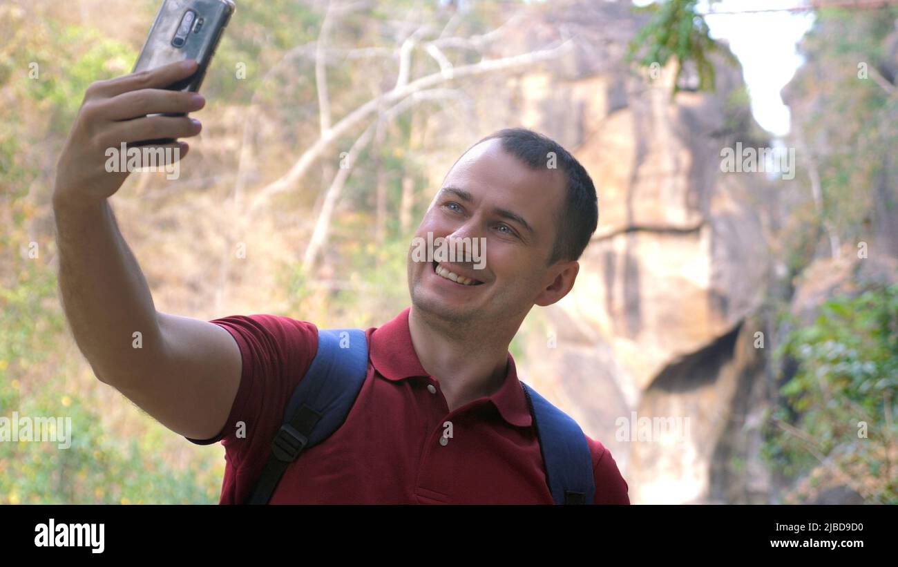 Un homme souriant prend ses selfies au téléphone contre un canyon dans un parc national. Le randonneur heureux enregistre des vidéos ou prend des photos avec la face avant Banque D'Images