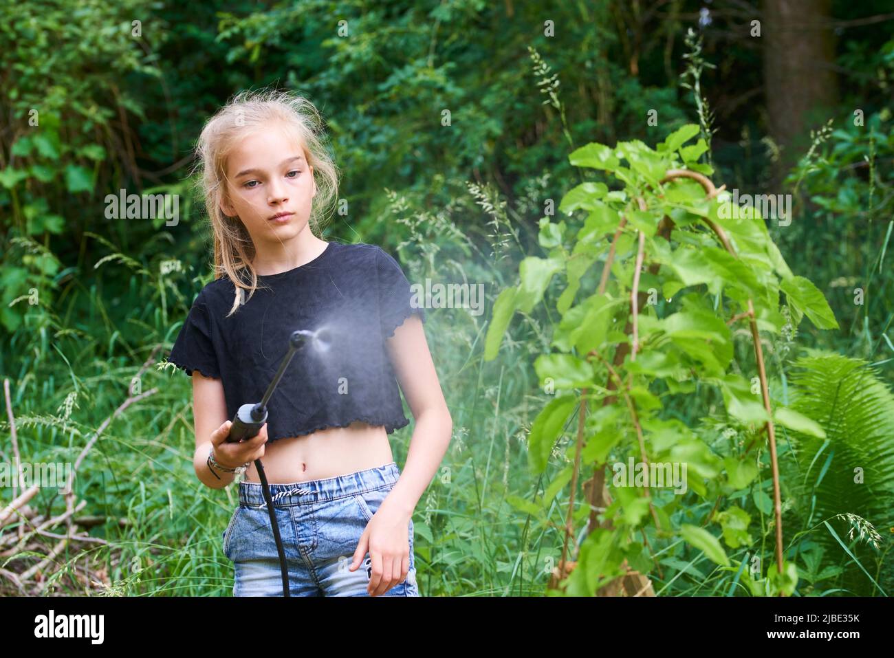 Une adolescente pulvérise un produit écologique contre les pucerons et autres ravageurs sur les arbres fruitiers et autres arbres dans le jardin et le verger. Mise au point sélective Banque D'Images