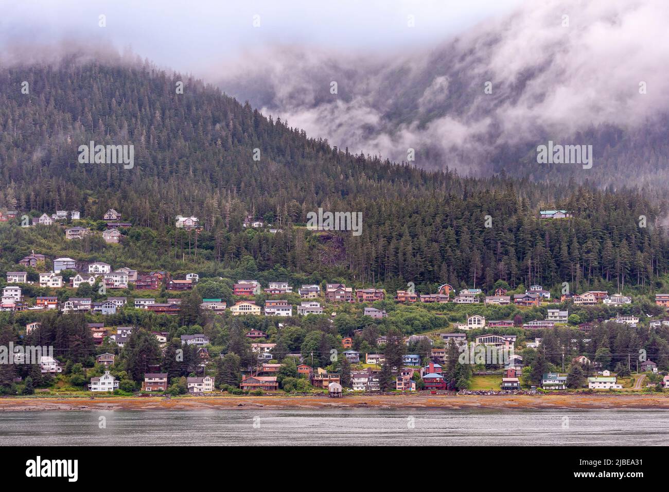 Juneau, Alaska, États-Unis - 19 juillet 2011 : rangées de maisons colorées le long de la rivage de l'île Douglas, au large du chenal Gasineau. Nuages gris bas sur la forêt de pins Banque D'Images