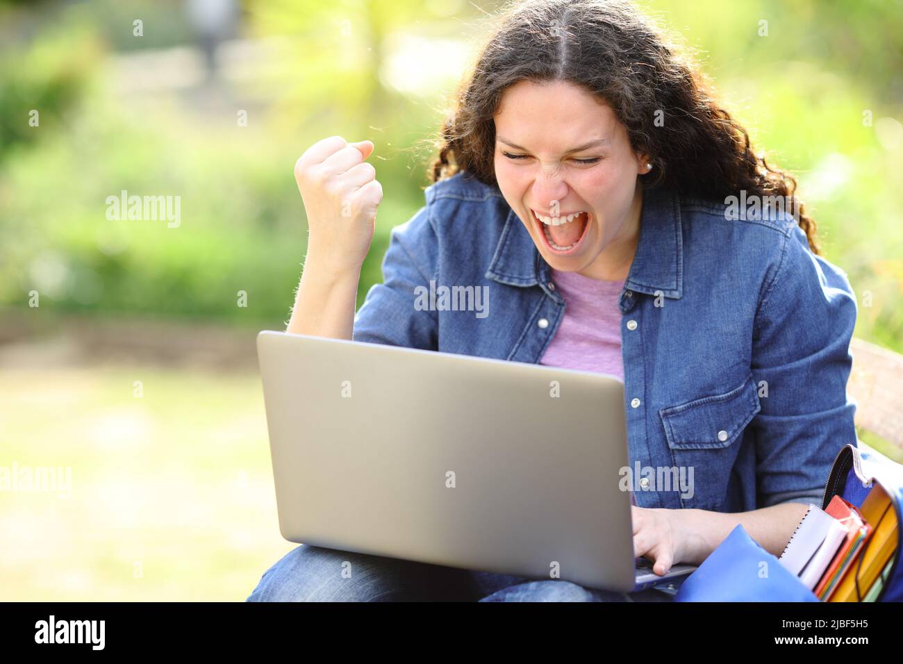 Une femme excitée qui vérifie le contenu d'un ordinateur portable dans un parc Banque D'Images