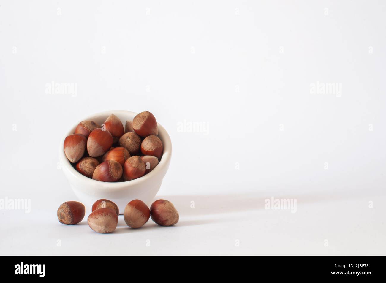 Noisettes, tas ou pile de fruits à coque avec shel dans une tasse blanche et certains sur fond blanc. Nourriture végétalienne saine et savoureuse, foyer isolé et sélectif. Banque D'Images