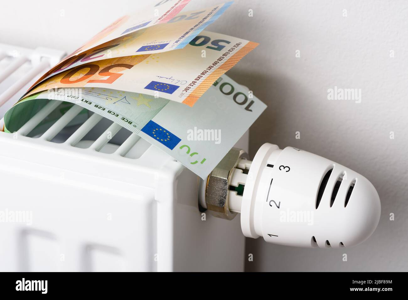 Billets en euros dans la batterie du radiateur de chauffage avec thermostat de température. Concept des coûts de chauffage coûteux et de la hausse de facture d'énergie pric Banque D'Images