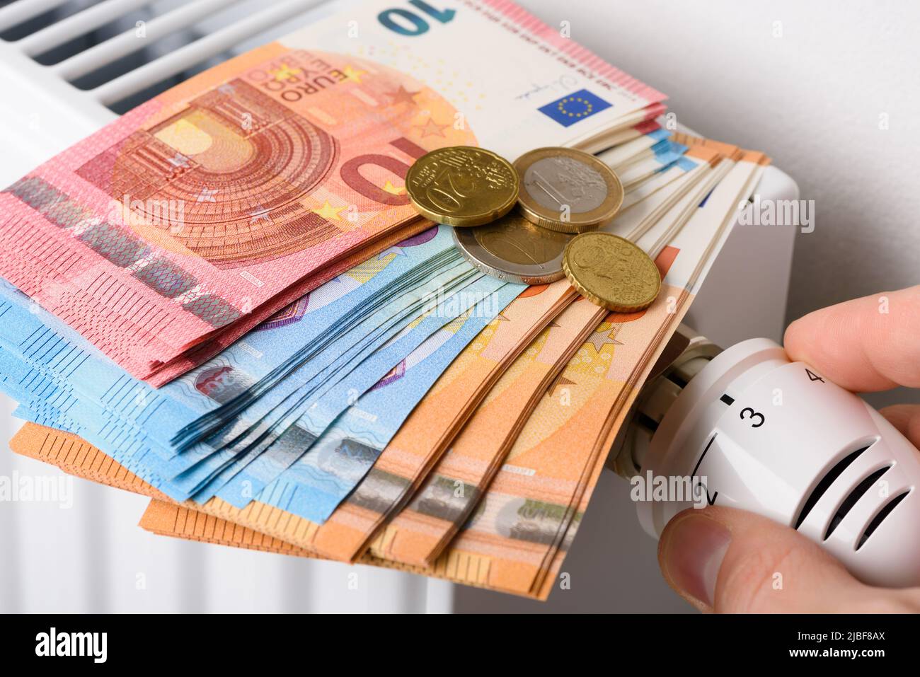 Réglage manuel du bouton de la vanne du thermostat de température du radiateur de chauffage avec une pile de billets en euros. Les coûts de chauffage coûteux et en hausse Banque D'Images