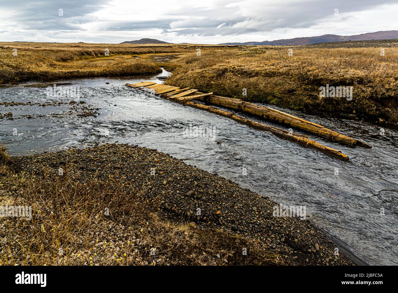 Un simple pont piétonnier fait de planches et de rondins traverse un ruisseau dans la lande près de Möðrudalur, dans l'est de l'Islande, un seul montagne conique visible à l'horizon. De tels ponts de fortune permettent aux randonneurs de traverser les rivières des hautes terres accidentées de l'Islande sans se mouiller les pieds. Banque D'Images