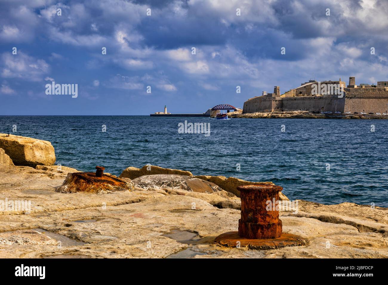 Île de Malte, vieux front de mer avec des bollards d'amarrage rouillés à Sliema avec vue sur le port de Marsamxett à fort St Elmo à Valletta. Banque D'Images