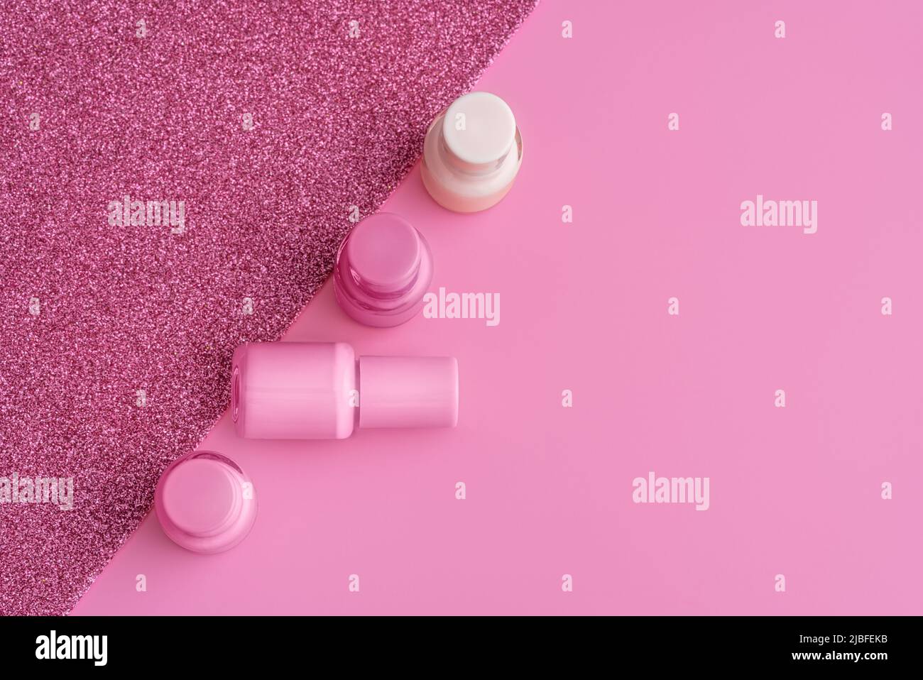 Modèle tendance avec flacons en verre vernis à ongles sur fond rose et étincelant. Concept de manucure. Maquette pour votre conception avec espace de copie. Style de pose à plat. Banque D'Images