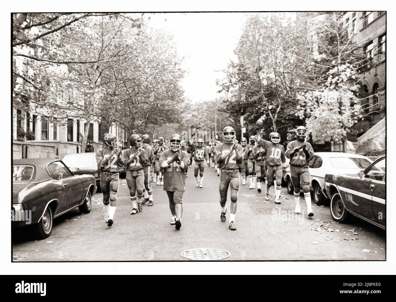 L'équipe de football John Jay H.S. s'y emmarche de son champ d'entraînement au chant et au clapping de l'école. Ils sont sous la direction de leurs cocapitaines. 1982, Brooklyn Banque D'Images