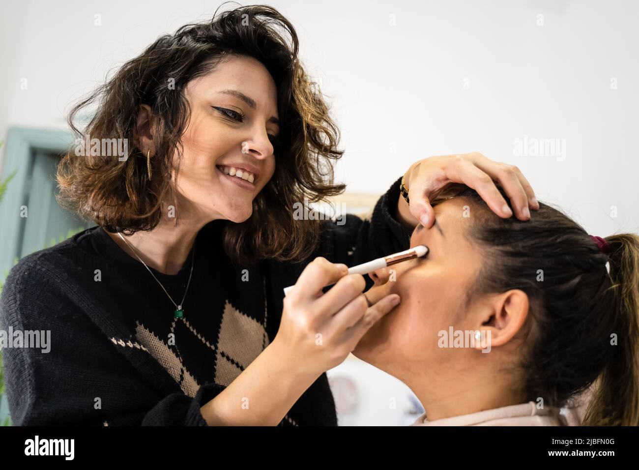 Gaie femme visagiste étalant fard à paupières sur la paupière de la femme pendant la séance de maquillage en salon Banque D'Images