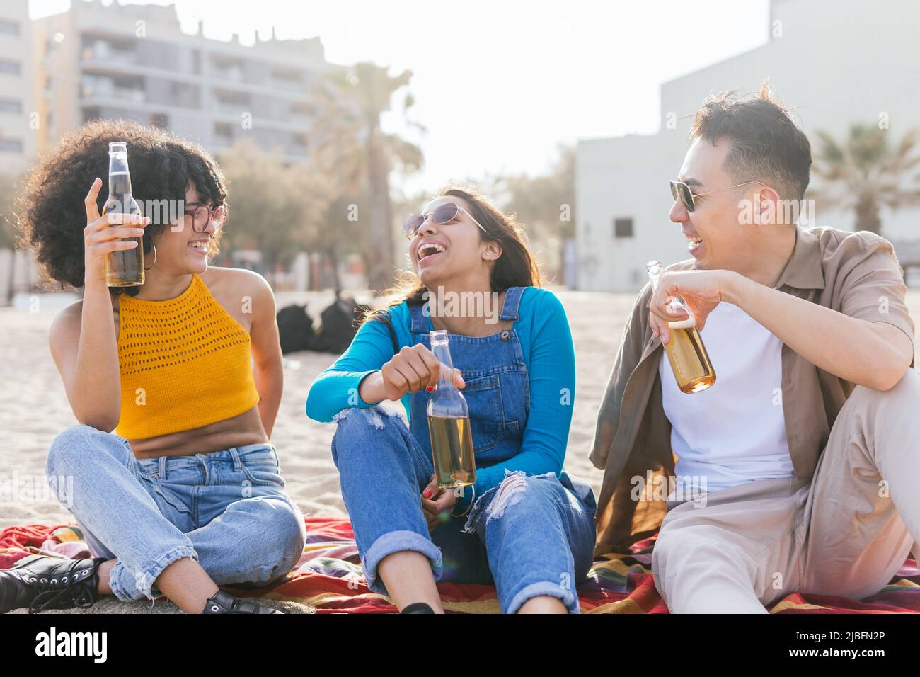Joyeux homme et femmes divers dans des vêtements décontractés boire de la bière et rire à la plaisanterie tout en passant une journée ensoleillée d'été sur la plage Banque D'Images