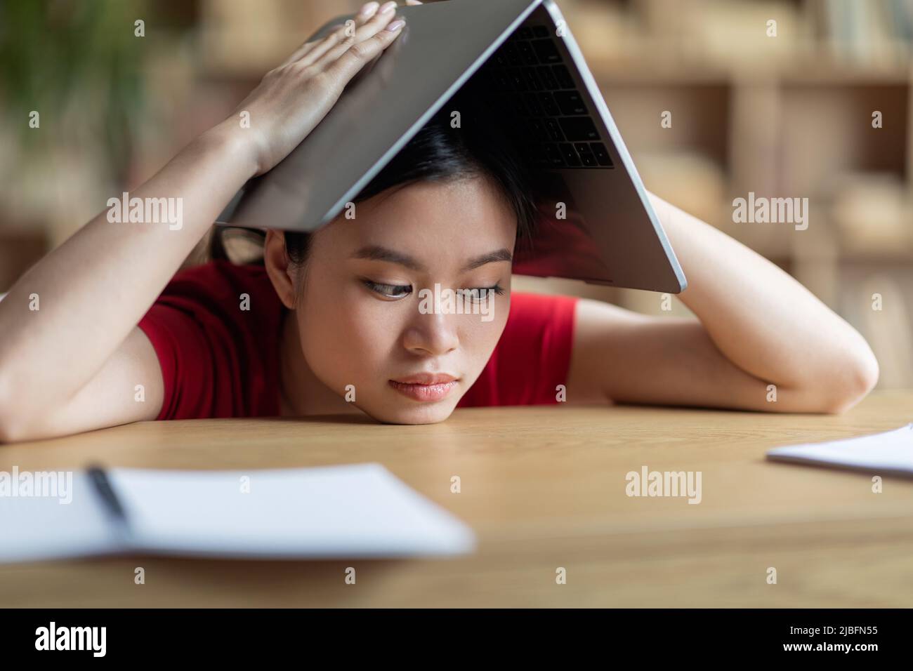 Fatiguée frustrée adolescente asiatique fait le toit avec le livre sur sa tête dans la bibliothèque ou l'intérieur de la chambre Banque D'Images