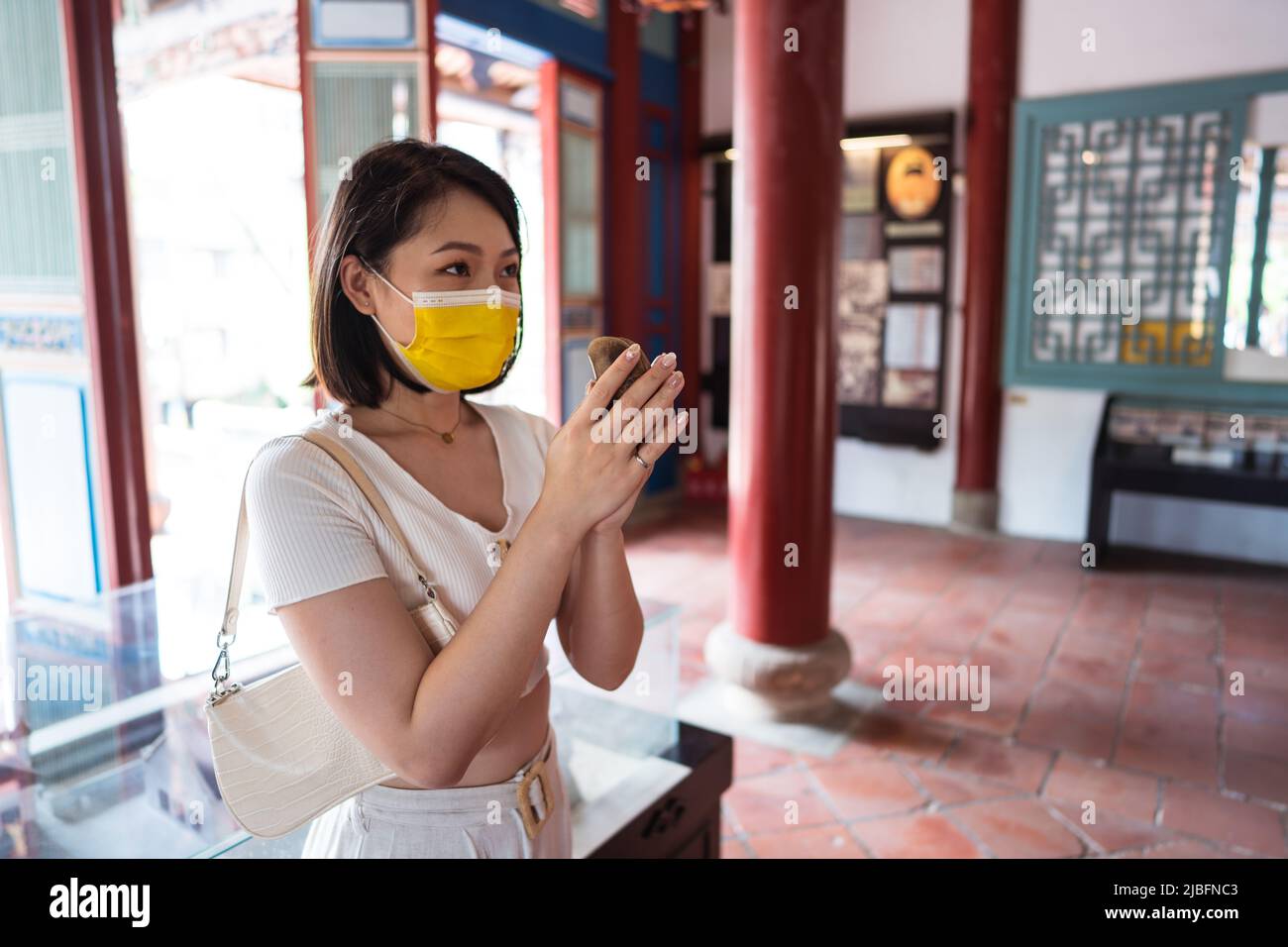 Jeune femme asiatique concentrée avec des cheveux foncés dans un petit top et un masque de visage tenant des blocs de lune dans les mains et regardant loin en se tenant debout à la température Banque D'Images