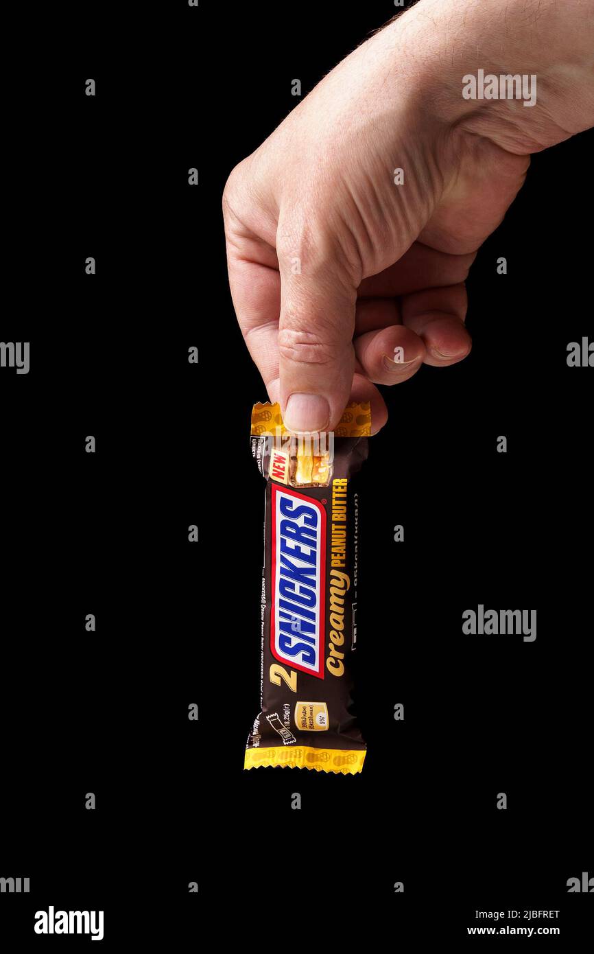 Barre de chocolat Snickers dans la main d'un homme gros plan, fond noir, vertical. Banque D'Images