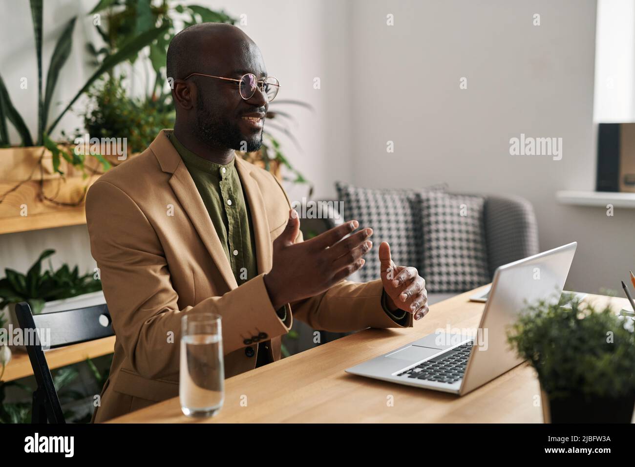 Jeune homme noir souriant en costume communiquant avec un patient en laine pendant une session psychologique en ligne tout en étant assis devant un ordinateur portable Banque D'Images