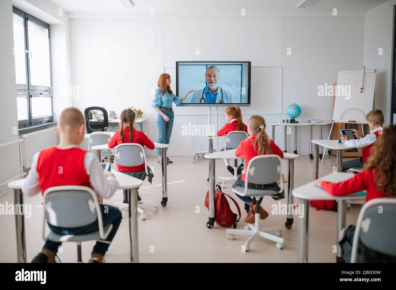 Vue arrière, classe d'élèves assis, à l'écoute de l'enseignant et à la lecture de cours en ligne avec le médecin en classe Banque D'Images