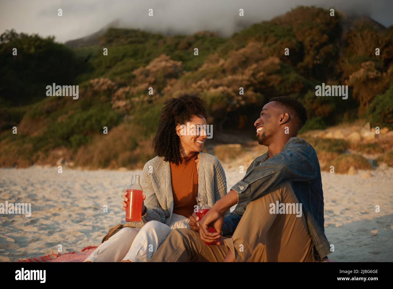 Rire jeune couple multiethnique se détendre sur une plage de sable au coucher du soleil Banque D'Images