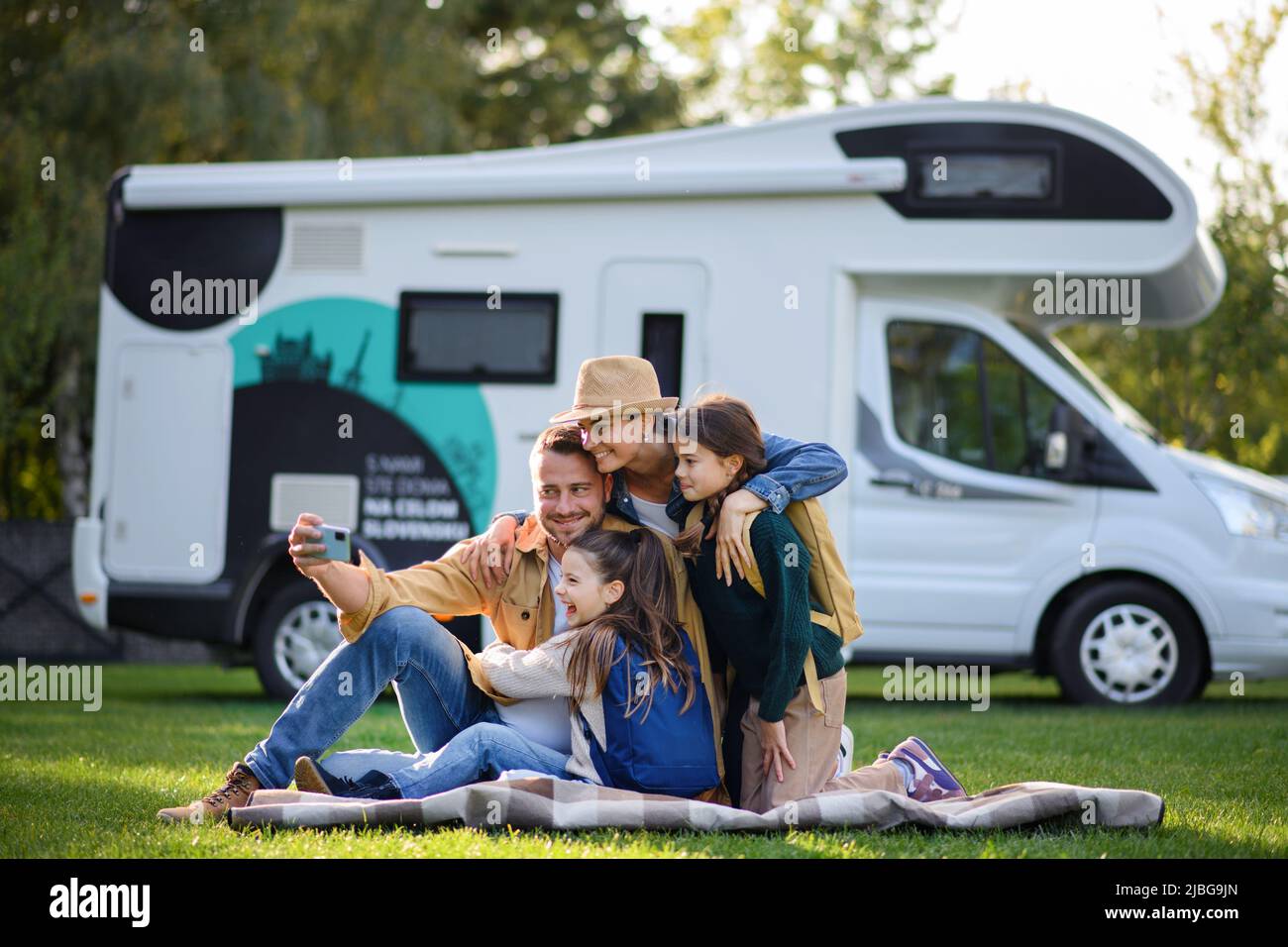 Une bonne famille avec deux enfants qui prennent le selfie avec une caravane en arrière-plan à l'extérieur. Banque D'Images