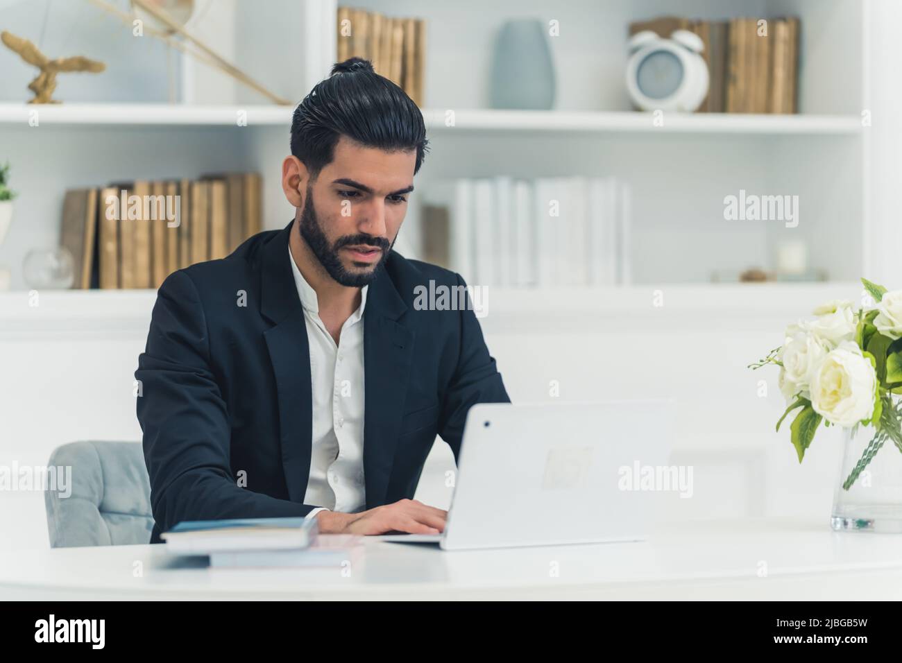 Photo en intérieur d'un jeune homme d'affaires cubain bien habillé, assis à un bureau, dactylographiant sur un ordinateur portable, en regardant focalisé. Photo de haute qualité Banque D'Images