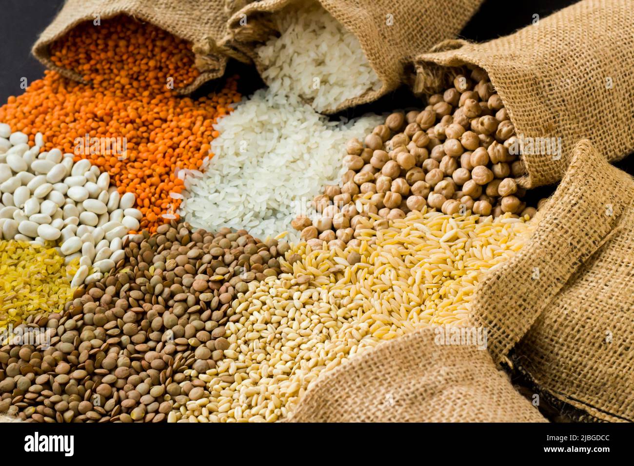 Lentilles rouges, pois chiches, riz blanc et bulgur versant du sac de jute sur la surface noire avec l'espace de copie. Concept de récolte Banque D'Images