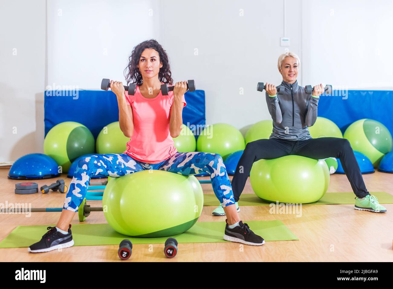 Les femmes de fitness s'exerçant assis sur des balles suisses vertes faisant des biceps assis courber des poids de levage pendant le train de groupe dans le club sportif. Banque D'Images