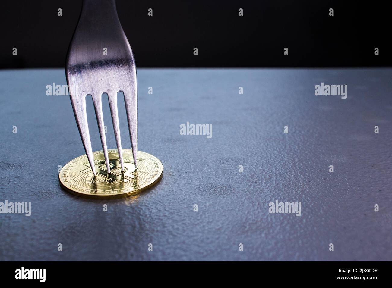 Image concept de la fourche dure Bitcoin (chaîne de blocs). La fourchette d'argent est un bitcoin doré. La pièce de monnaie crypto-monnaie sous la fourchette est sur la table dans l'obscurité. Banque D'Images