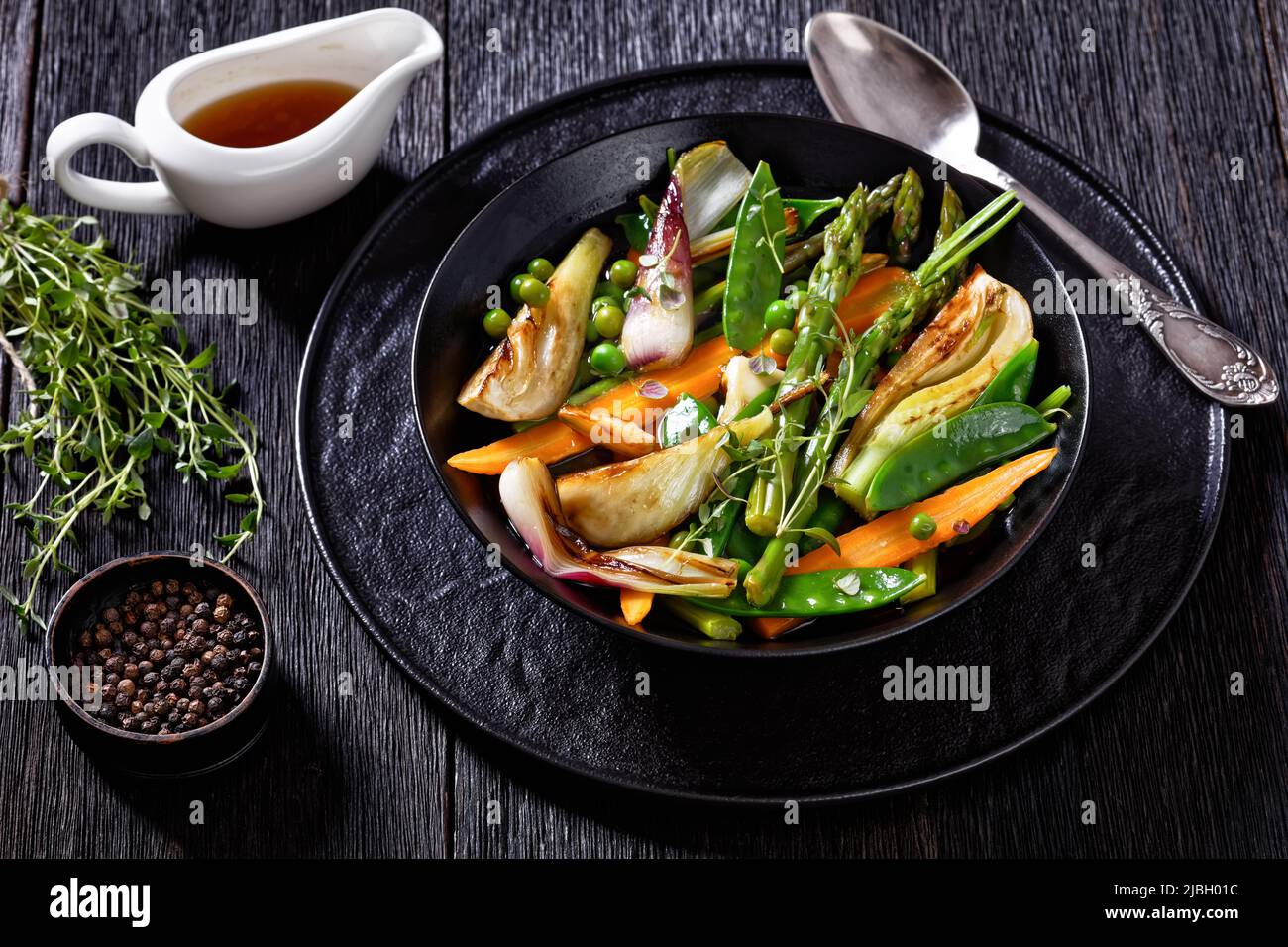 Barigoule de légumes de printemps, fenouil, carottes, pois mange-tout, pois verts, asperges avec bouillon de légumes dans un bol noir Banque D'Images