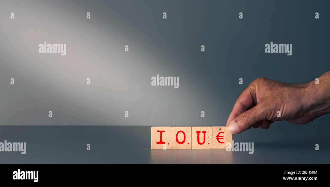 Concept de la dette ou de l'argent dû, la main posant des blocs boisés avec I,O,U Banque D'Images