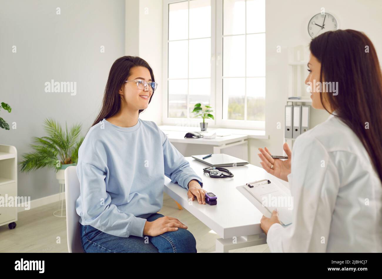 Le médecin parle à une jeune patiente qui utilise l'oxymètre de pouls du bout des doigts dans un cabinet médical. Banque D'Images