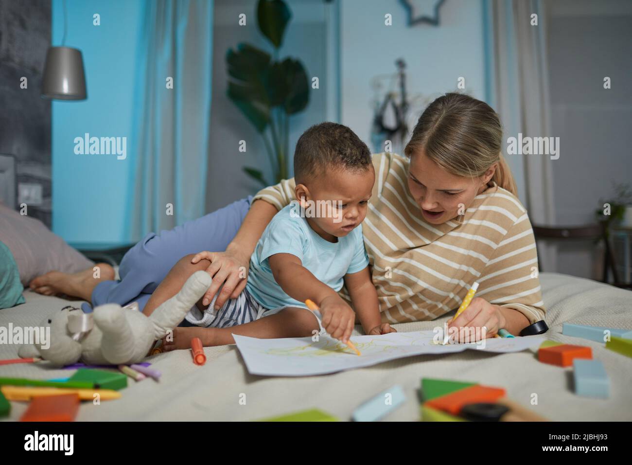 Portrait d'une mère caucasienne heureuse avec un joli dessin de bébé de race mixte allongé sur le lit Banque D'Images