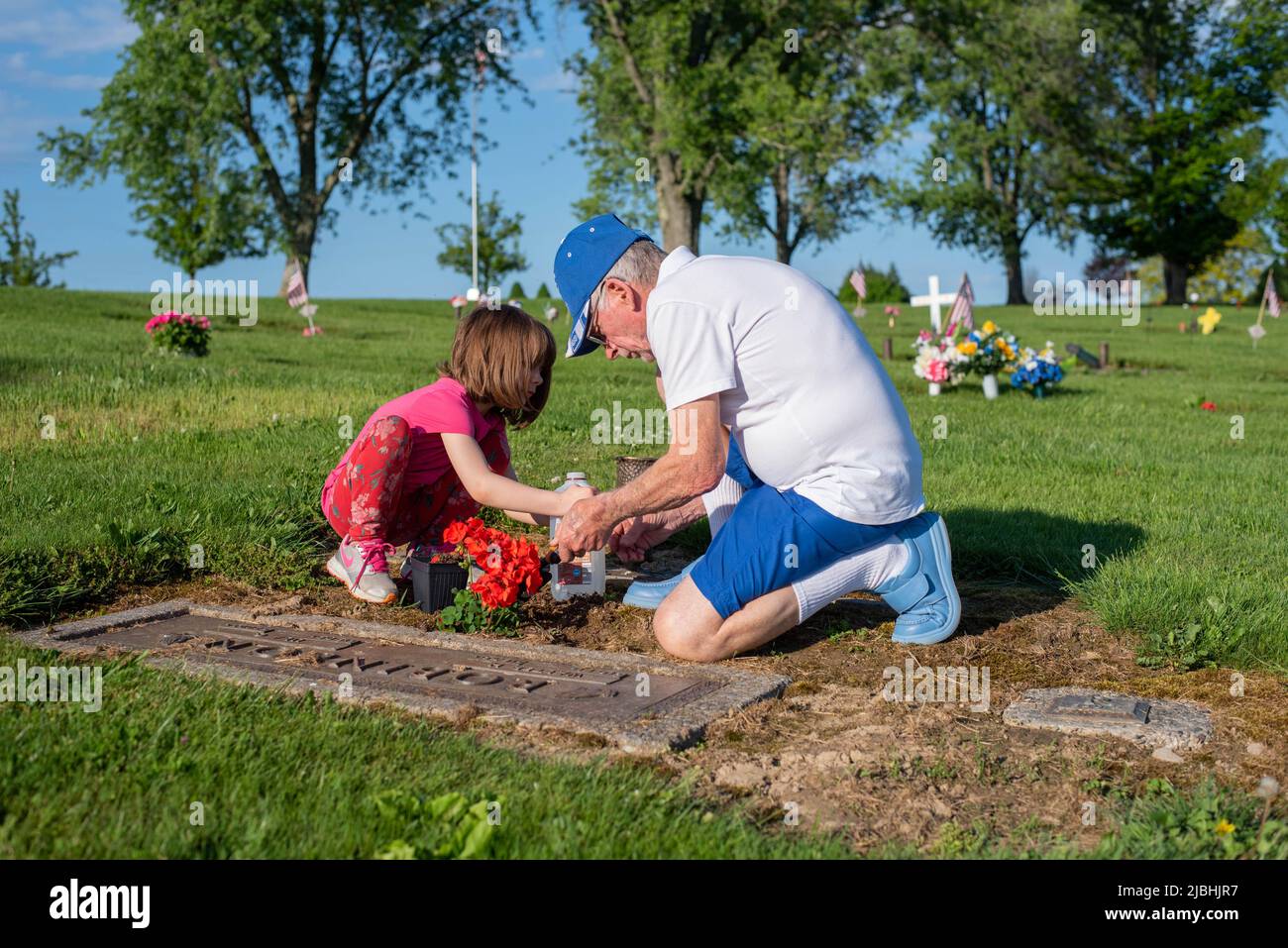 Un homme et sa petite-fille décorent une pierre tombale dans un cimetière le jour du souvenir. Banque D'Images