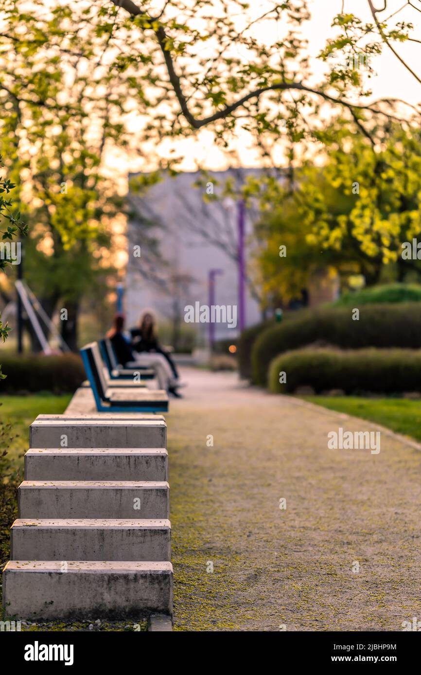 Un banc vide dans un parc de la ville baigné dans la lumière orange du soleil couchant. Certaines personnes se détendent à distance Banque D'Images