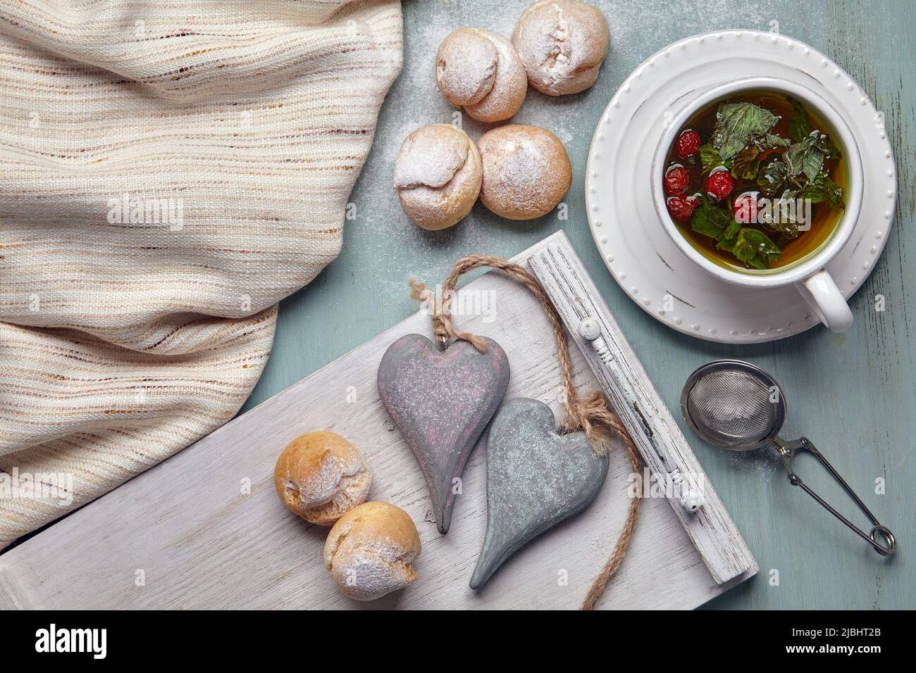 De délicieux profiteroles à la crème fouettée et deux coeurs décoratifs en bois arrosé de sucre en poudre, avec une tasse de tisane et une serviette de thé sur Banque D'Images