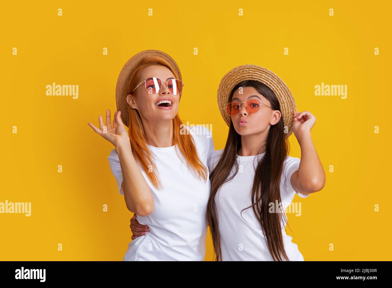 Studio portrait d'enfant drôle avec maman. Bonne fille et mère élégante posant sur fond jaune studio, portant un chapeau de paille et des lunettes de soleil Banque D'Images