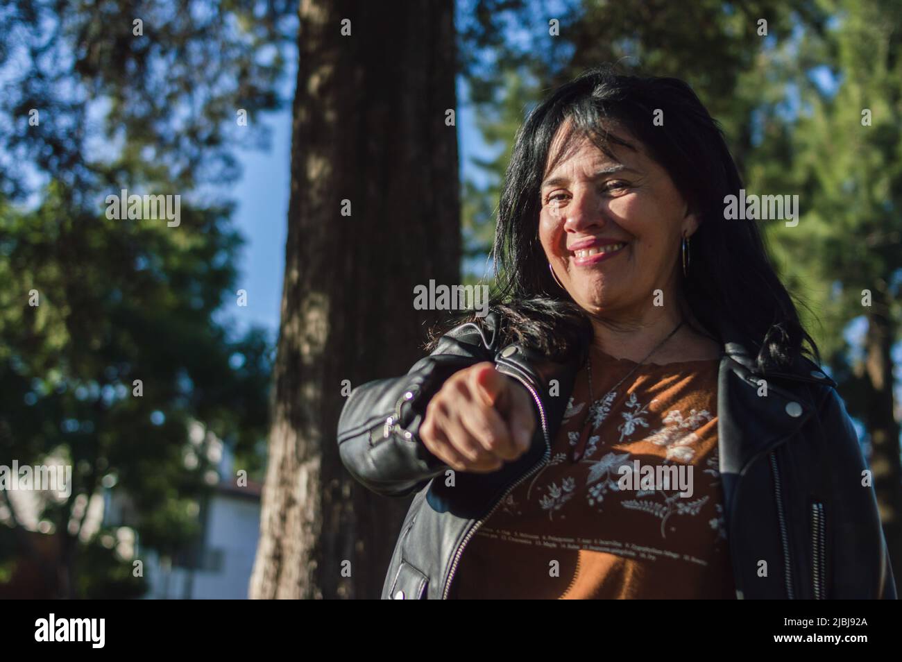 portrait latin caucasien femme adulte, à l'extérieur dans la campagne, debout souriant et pointant le doigt vers l'appareil photo, copier l'espace vers la gauche. Banque D'Images