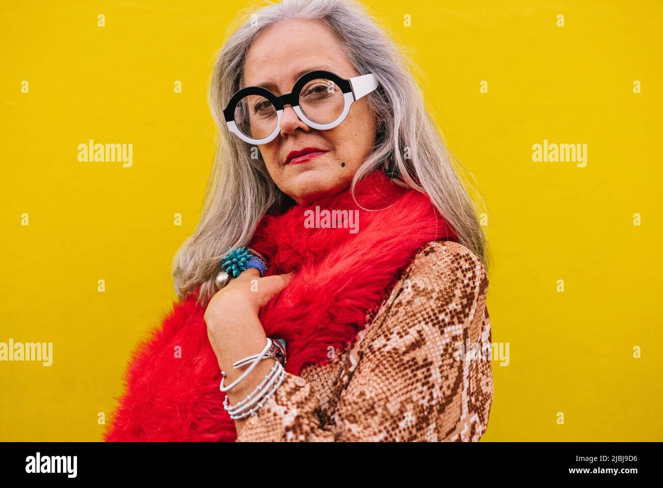 Femme âgée regardant la caméra tout en se tenant contre un fond de citron. Femme âgée élégante, pleine de confiance et de jeunesse, vêtue d'un rouge Banque D'Images
