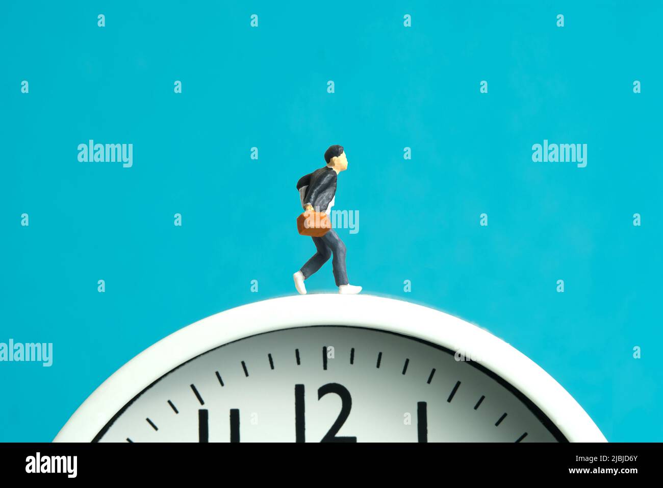 Photographie miniature de personnage de jouet de personnes. Fin et début de l'école concept. Jeune homme élève courant au-dessus de l'horloge blanche isolée sur fond bleu. Image Banque D'Images