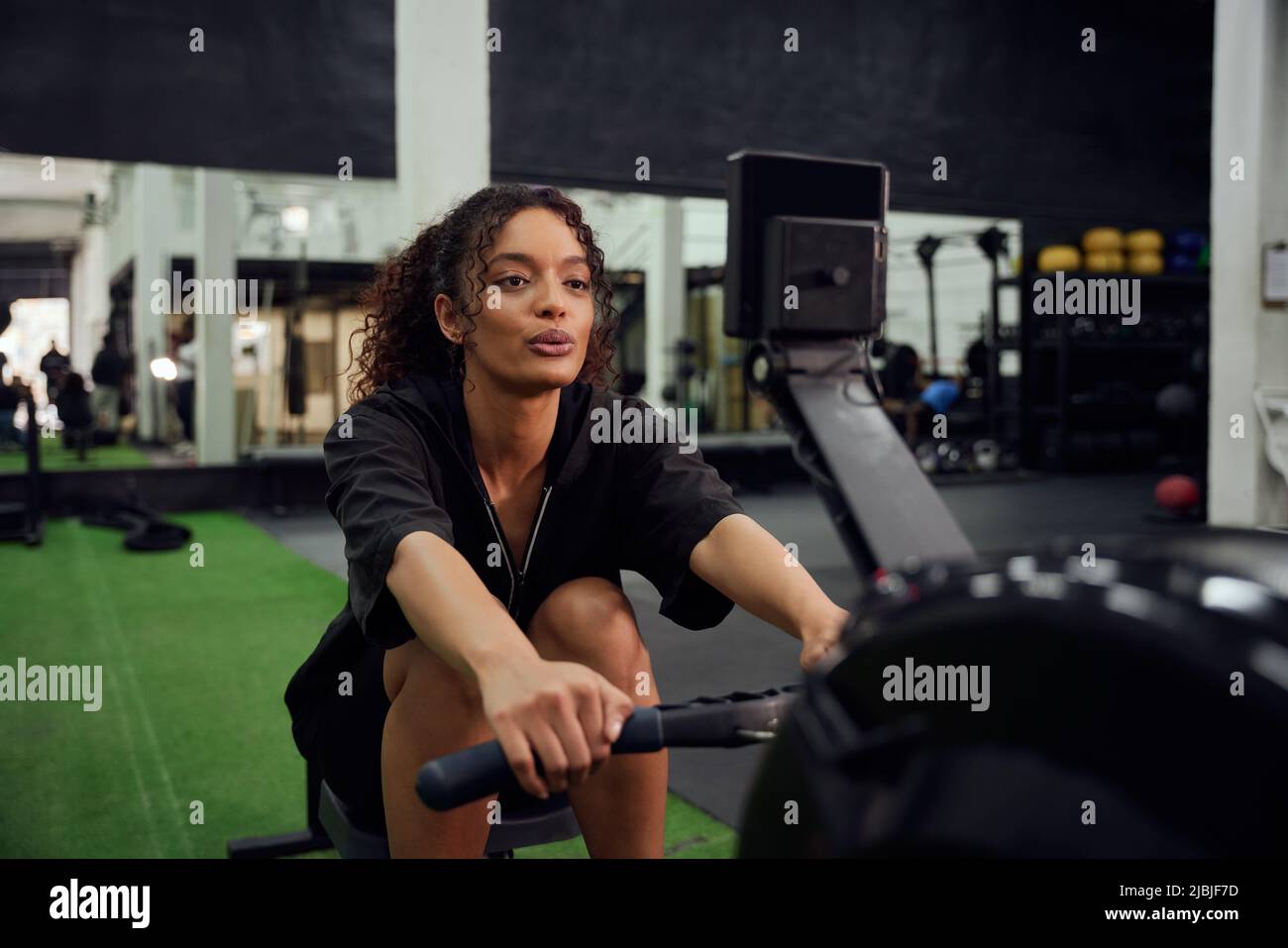 Femme afro-américaine utilisant une machine à ramer pendant l'entraînement en cross-fit. Une athlète féminine s'entraînant intensément dans la salle de sport. Photo de haute qualité Banque D'Images