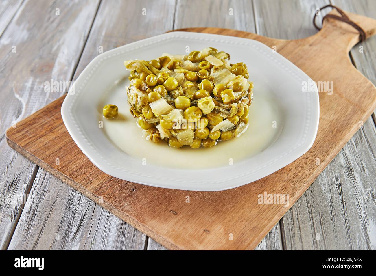 Petits pois cuits avec des cœurs de laitue sur une assiette blanche. Cuisine gastronomique française Banque D'Images